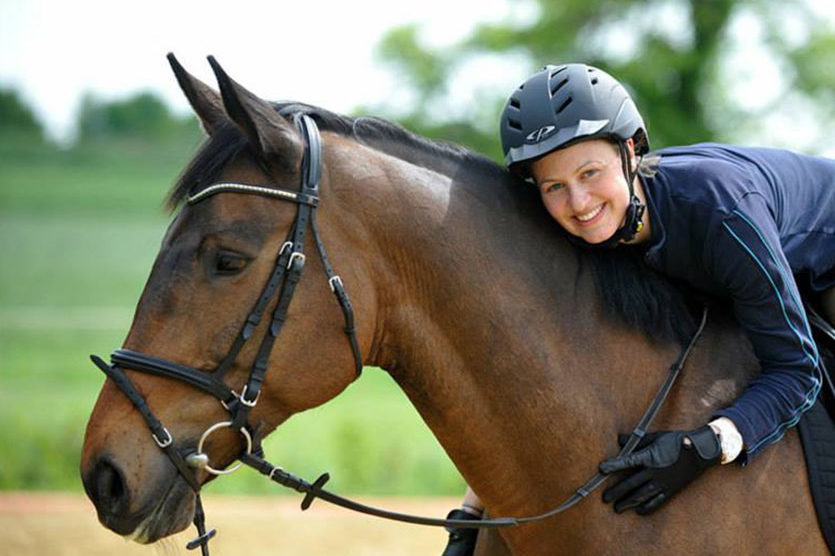 Reiterin sitzt auf braunem Pferd und lehnt sich liebevoll über den Hals